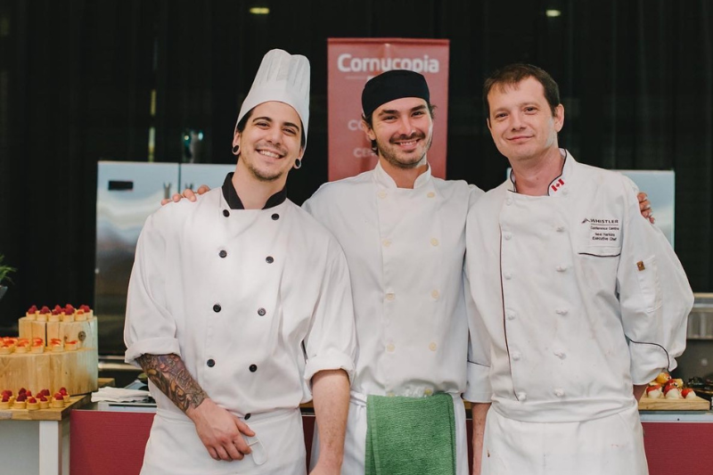 Three men dressed in chefs attire in front of a Cornucopia sign
