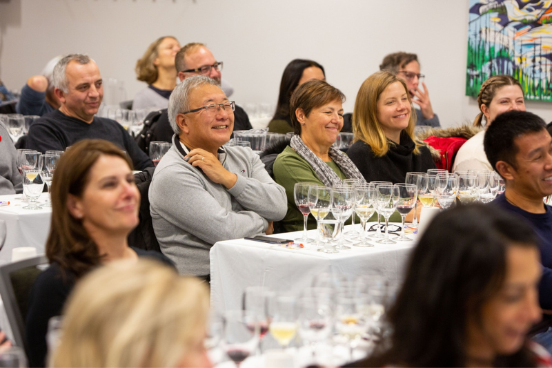 A large group of people sitting classroom style in a room doing a wine seminar