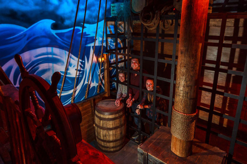 Three people inside an escape room themed as a pirate ship.