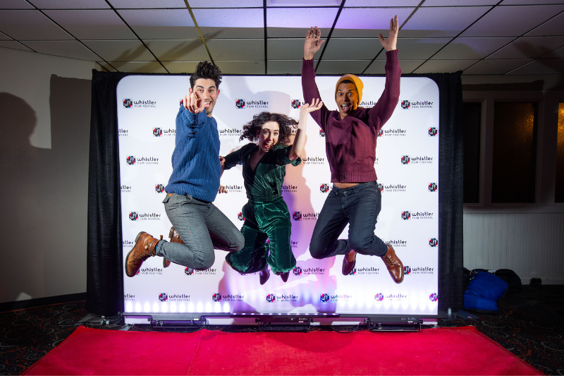 Three people jumping with joy in front of a film premier screen