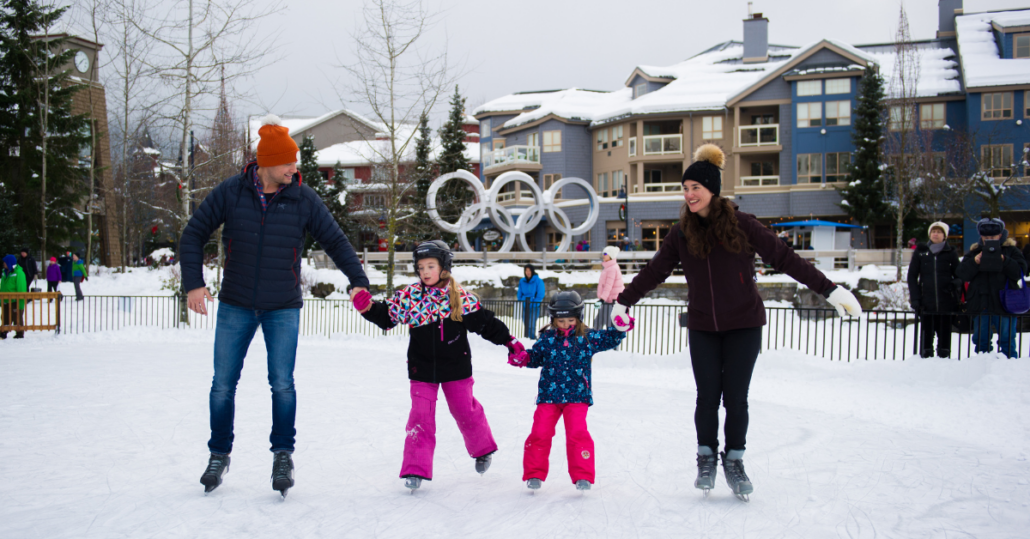 Dad, daughter, son and mother ice skating in front of the olympic rings in whistler village