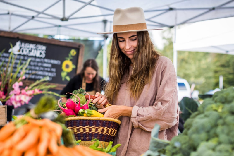 Lady gathering vegetables at a farmers market wearing a nice hat
