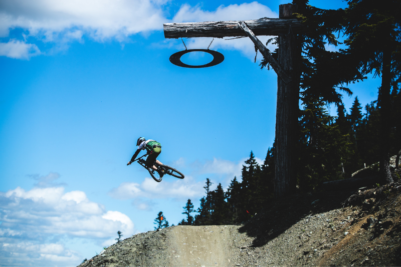 Person flying through the air on a mountain bike doing a jump stunt beside an Oakley sign at the Whistler Mountain Bike Park nearby to Whiski Jack Resorts Whistler